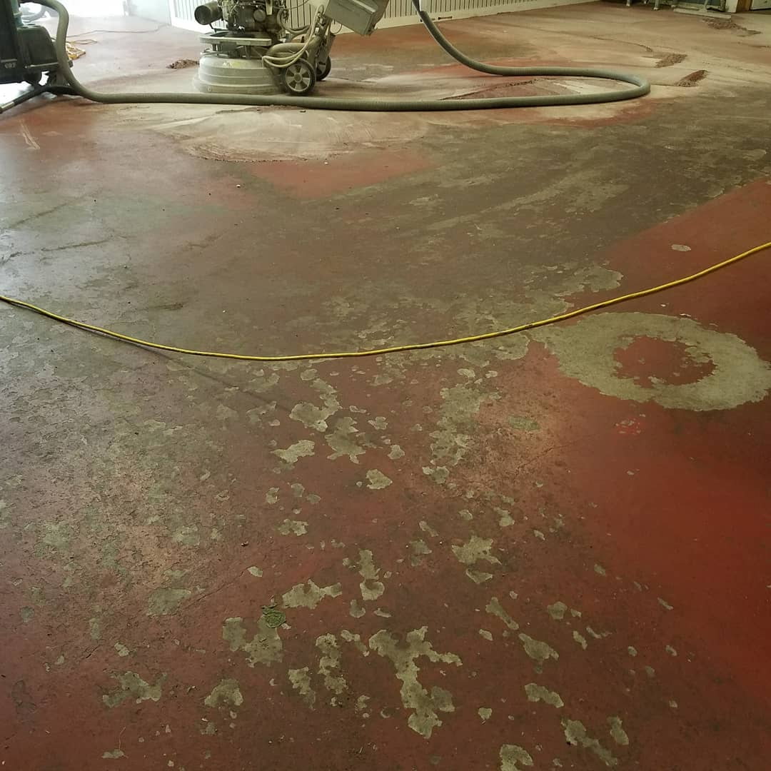 Worn red concrete floor being diamond-ground for epoxy prep